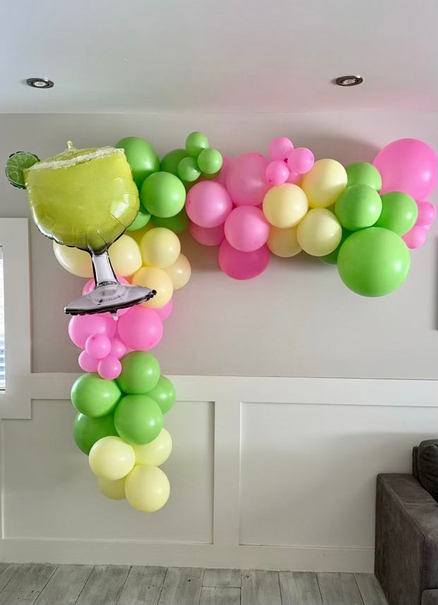 A pink green and yellow balloon arch backdrop with a margarita glass balloon