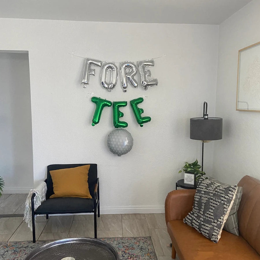 Living room with 'FORE TEE' balloons on the wall, brown couch, and black chair.